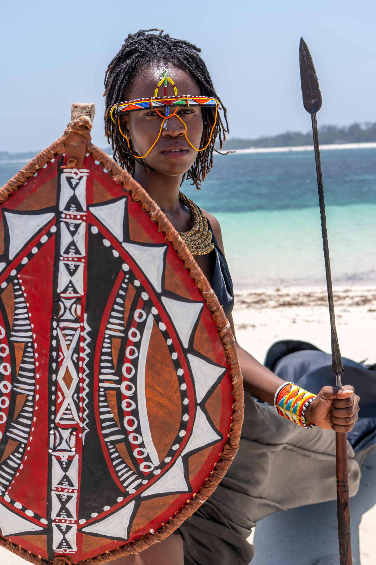 Portrait with traditional beaded adornments, shield and spear beside the ocean