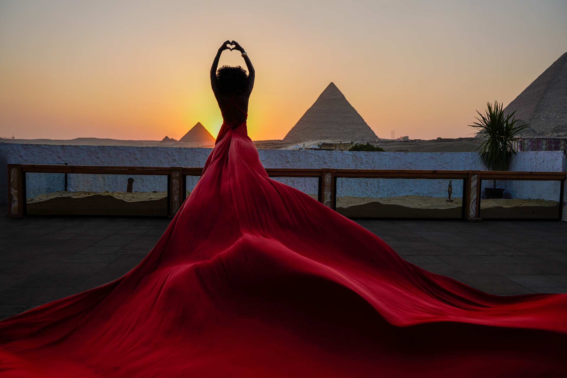 Silhouette in a red flying dress forming a heart against the Giza sunset from a rooftop