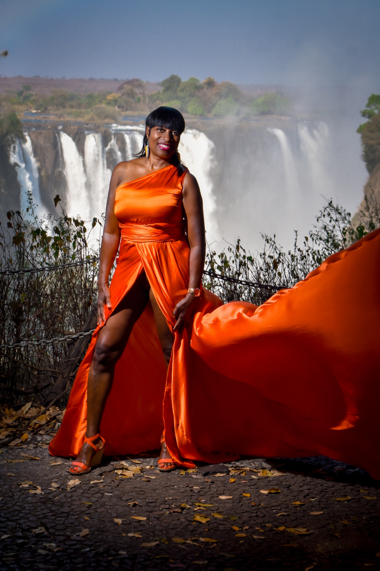 One-shoulder orange flying dress in front of the falls spray