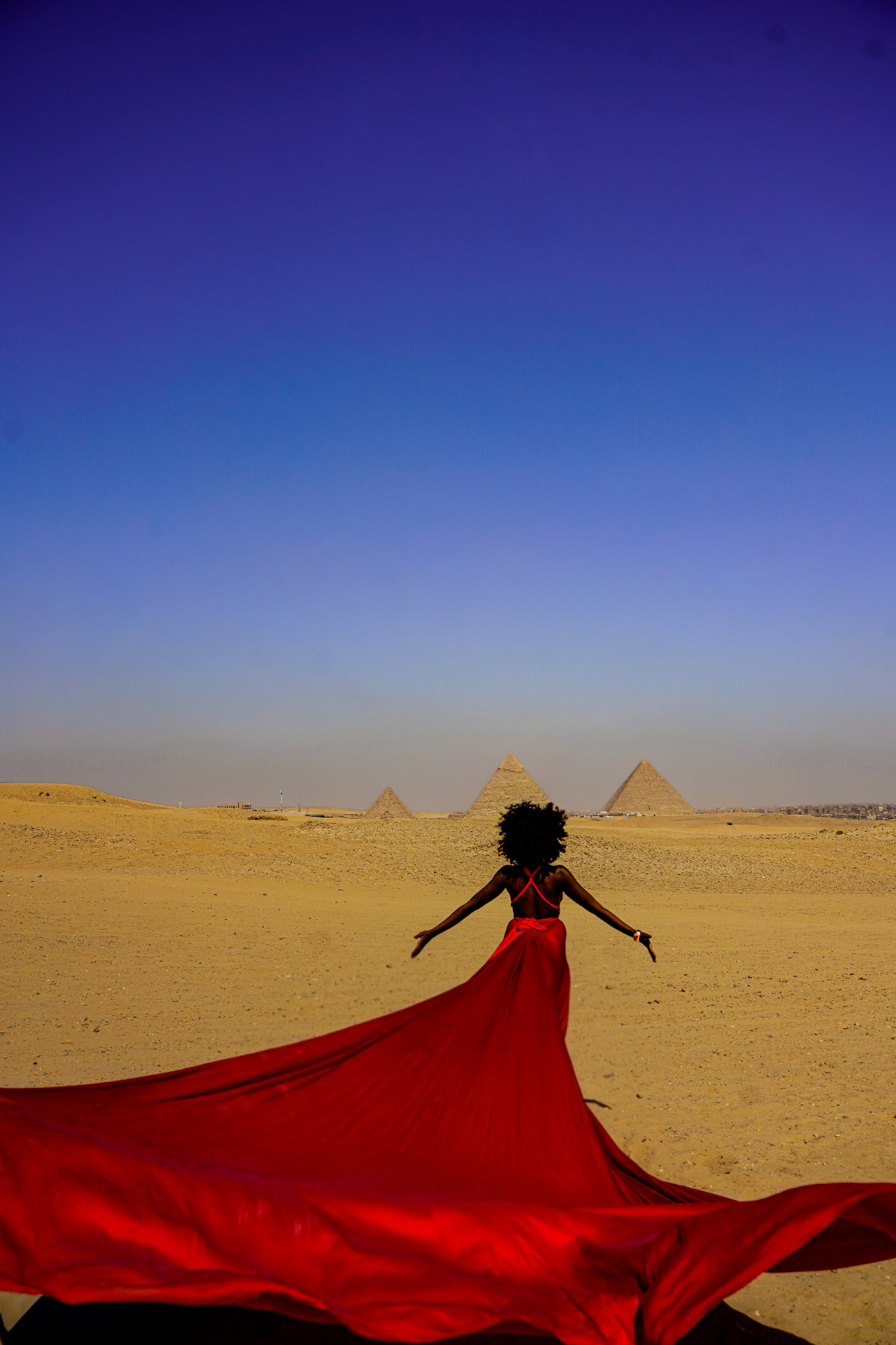 Woman in a red flying dress with arms outstretched in the desert before the Pyramids of Giza — locations on request