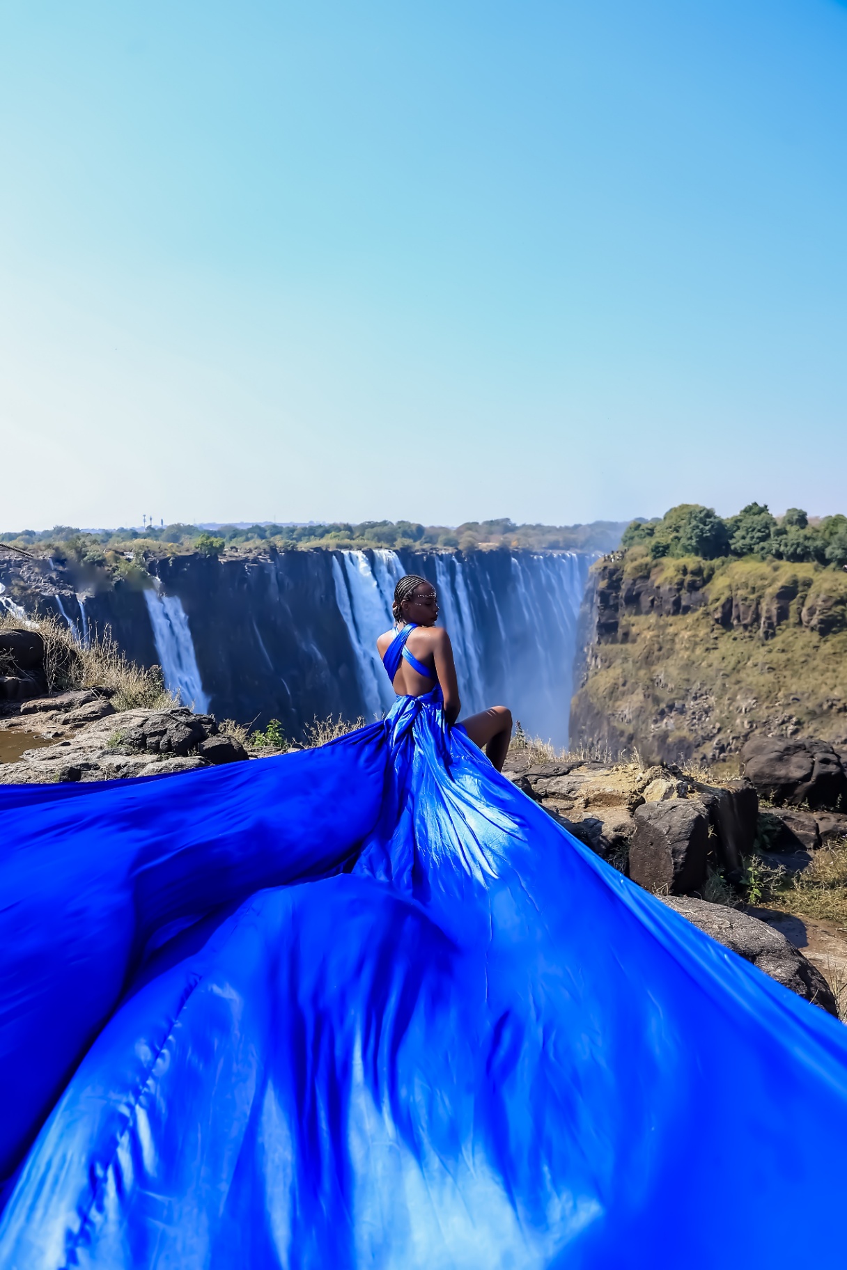 Royal blue flying dress spread over the rocks at the edge of the falls gorge